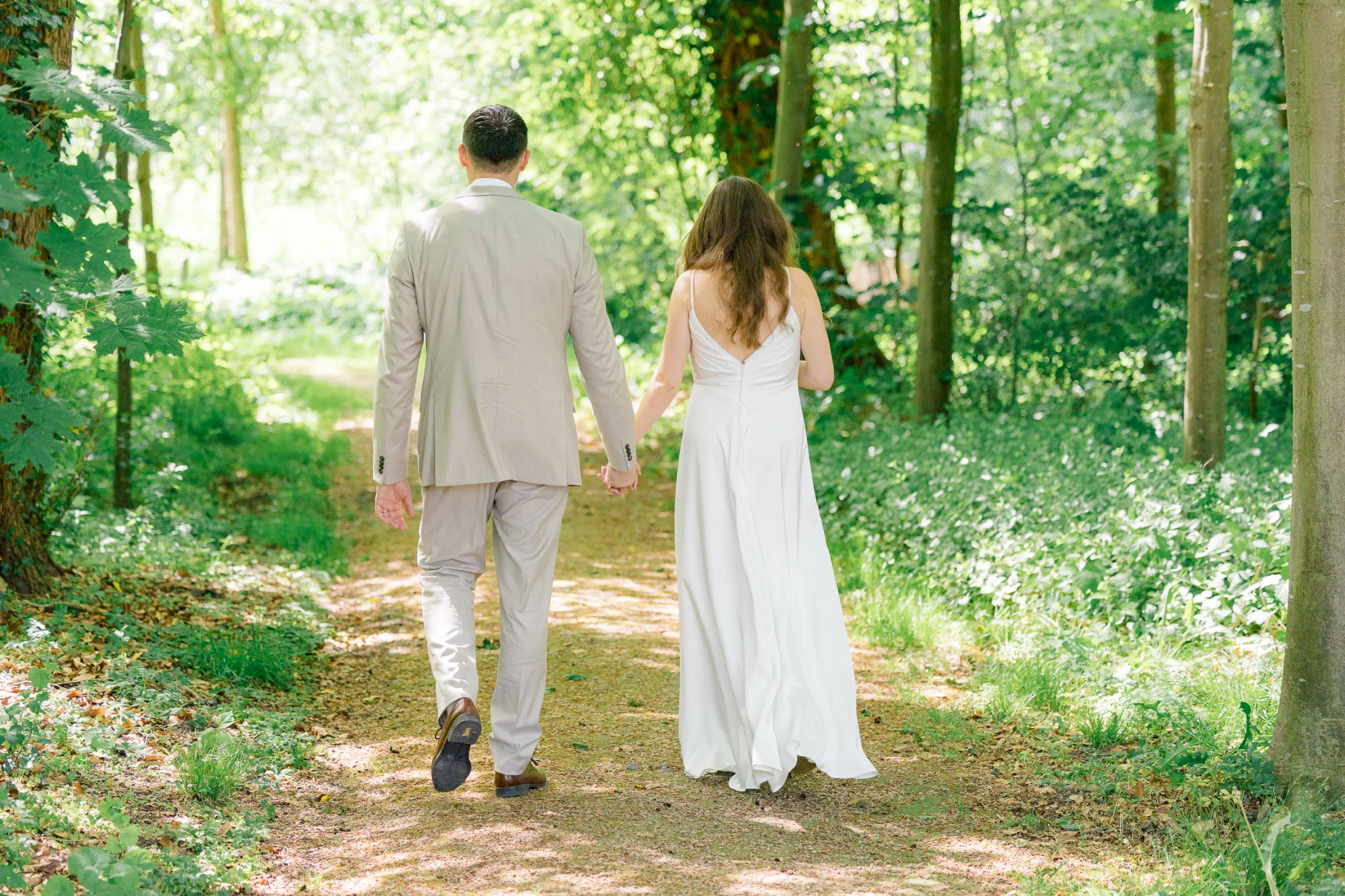 Ein Brautpaar geht Hand in Hand auf einem Waldweg.
